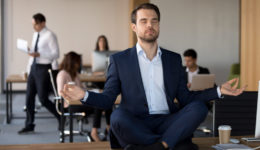 Businessman in suit sitting on table and meditating in office