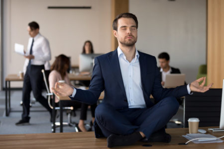 Businessman in suit sitting on table and meditating in office
