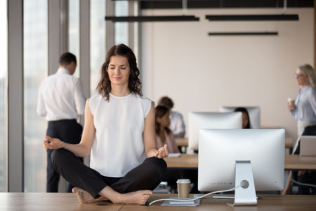 Calm female employee practice yoga on table in coworking space